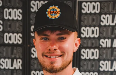 Young man wearing a black SOCO hat stands in front of a background with repeating “SOCO SOLAR” text.