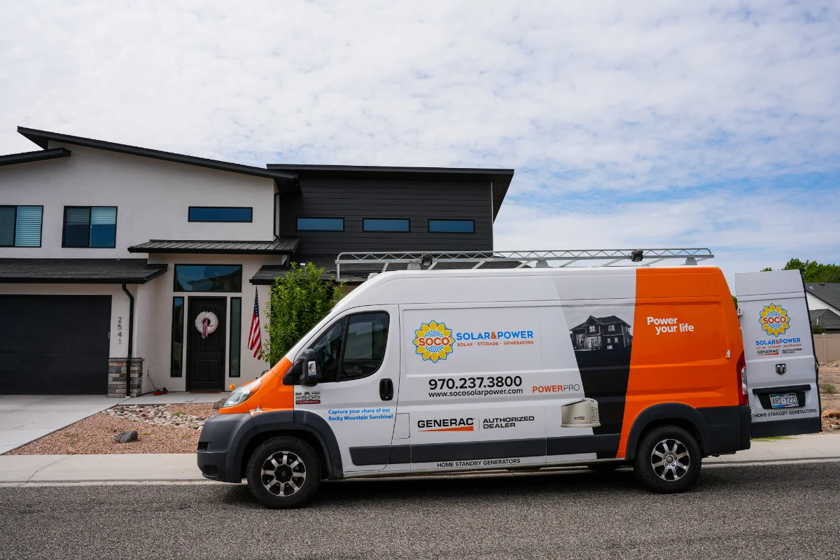 A white and orange SOCO Solar Power van is parked on a residential street in front of a modern two-story house.